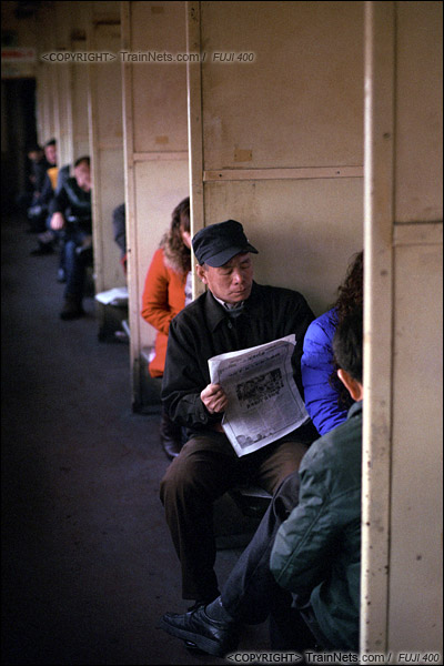 2014年2月。甘粛省の白銀鉱山鉄道、354番通勤車。朝、山から出る車両で、一人の勤労者が新聞を読んで時間をつぶしている。この22型客車は、最も原始的な木製の设备、インテリアのままだ。（E4034）