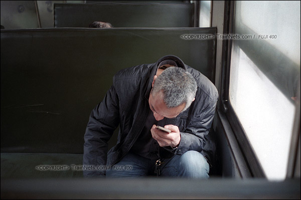 2015年1月。甘肃省白银铁路。下午，355次通勤车，一位乘客坐在车里看手机打发时间。（F0615）