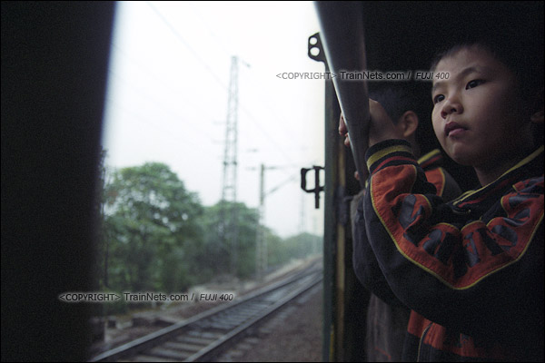 2007年2月，广州。清晨，开往广州市区的棚车通勤列车，一位孩子扶着栏杆看风景。（A7524）